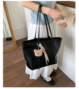 Black crocodile embossed tote bag with plush bear charm worn by a model in a minimal room