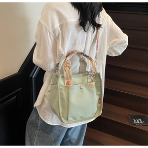 Detail of light green canvas tote bag featuring floral embroidered handles and crossbody strap