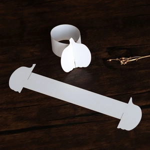 Macro detail of white paper pumpkin napkin ring with interlocking clasp on wooden surface