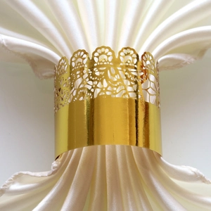 Close-up of golden laser-cut floral napkin ring on a white satin cloth for wedding decor