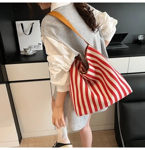 Detail of red and white striped tote bag with brown leather handles worn by a model