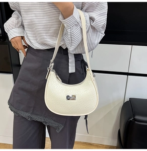 Detail of cream-colored crescent bag with faux crocodile texture and silver logo plate