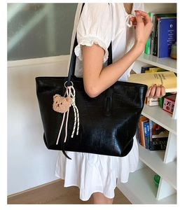 Detail of black faux crocodile tote bag with plush bear charm worn by a model