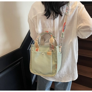 Detail of light green canvas tote bag with floral straps and side pockets in daily use