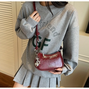 Detail of burgundy leather crescent bag featuring a silver bear charm and knot strap
