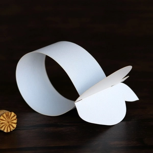Close-up of a white paper napkin ring with a butterfly cut-out on dark wood background