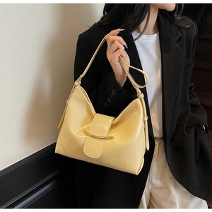 Detail of cream yellow leather bag featuring a polished gold curved metal ornament