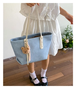 Detail of light blue crocodile embossed tote bag with contrast white handle and bear charm