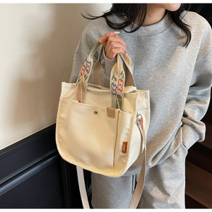 Detail view of canvas tote bag with floral embroidered strap and metal snap pocket