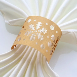 Detail of champagne gold snowflake laser-cut paper napkin ring on white silk cloth
