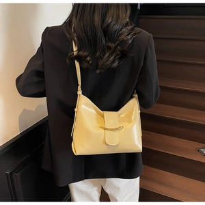 Minimalist creamy yellow patent leather crossbody bag with golden crescent buckle detail