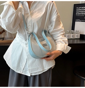 Close-up of woven light blue and silver crescent bag with metallic logo and strap
