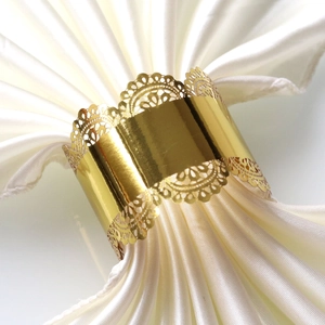 Macro shot of gold laser-cut lace napkin ring on white satin fabric for hotel wedding