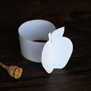 Detail of white paper napkin ring with 3D apple cutout on a rustic wooden background