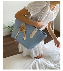 Sky blue tote bag detail with brown plush bear charm and leather handles on white dress