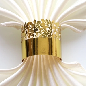Detailed view of shiny gold leaf cutout napkin ring on a white satin cloth for parties
