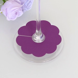 Detail view of purple flower-shaped paper place cards on wine glass stems for parties