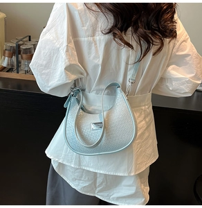 Detail of light blue hobo bag with woven texture and silver logo plate on model