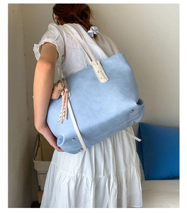 Detail of light blue croc-embossed tote bag with bear charm worn by a model