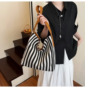 Detail of striped canvas tote with brown leather shoulder strap in a minimalist setting