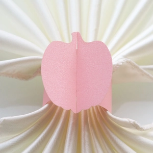 Close-up of pink pearlescent paper napkin ring in a festive pumpkin shape on white satin