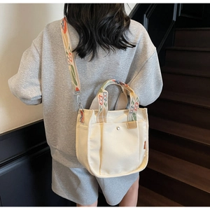 Detail of beige canvas tote featuring floral embroidered handles and adjustable strap