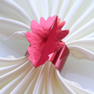 Détail d'un rond de serviette en métal rouge en forme de feuille sur tissu de soie