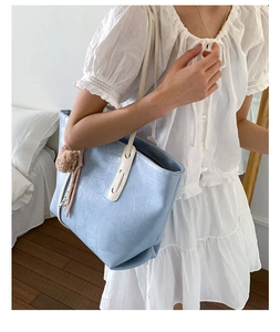 Light blue faux croc tote bag with plush bear charm and ribbon detail on a white dress