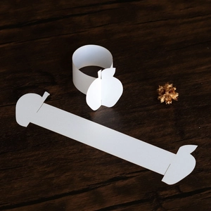 Detail of white apple-shaped paper napkin ring on a dark rustic wooden background