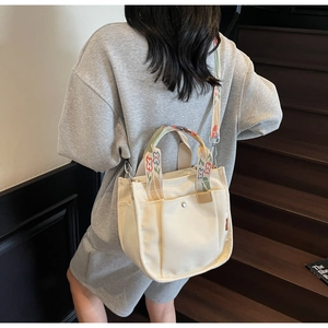 Detail of canvas tote bag with multi-color floral embroidery on handles and straps