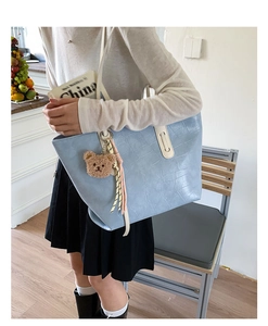 Detail of light blue tote bag with crocodile pattern and bear charm on shoulder