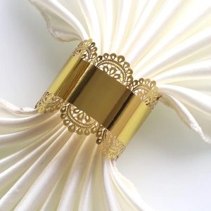 Detail of golden cutout lace napkin ring with elegant floral pattern on white silk fabric