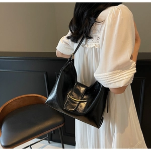 Close-up of black glossy leather tote bag with gold curved metal detail and slim strap