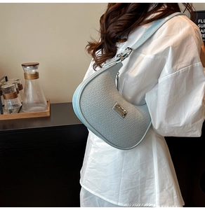 Detail of light blue hobo bag with woven texture worn by a model in a white shirt