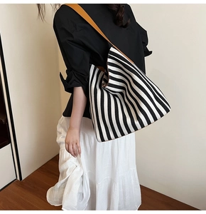 Detailed side view of large striped canvas tote bag with brown leather shoulder straps