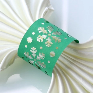 Close-up of green laser-cut snowflake napkin ring on a white satin napkin