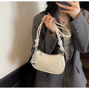 Detail of a creamy white crescent bag featuring crinkled patent leather and silver charms