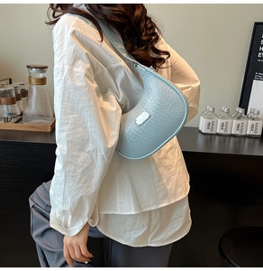 Detail of light blue woven hobo bag with silver logo plate shown on model