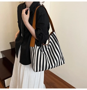 Detail of striped canvas tote bag featuring premium brown leather shoulder straps