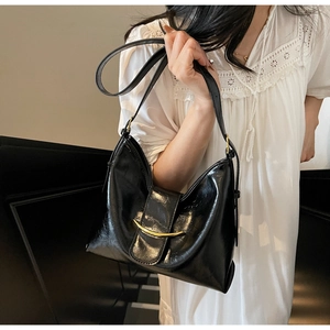 Detail view of black glossy shoulder bag with vintage gold metal buckle on white lace dress