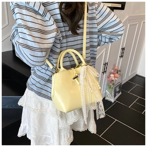 Fashionable pale yellow crossbody bag featuring a large pearl lace bow and smooth finish