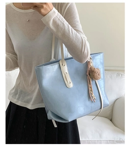 Detail of light blue croc-embossed tote bag with cream handles and plush charm accessory