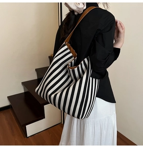 Detail of striped canvas tote bag with brown leather shoulder strap shown on model