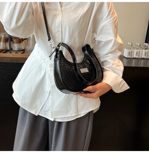 Detail of black woven crescent bag featuring silver logo plate and sleek chain strap