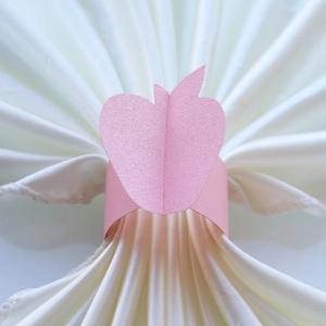 Detailed top view of pink apple-shaped paper napkin ring on elegant white pleated fabric