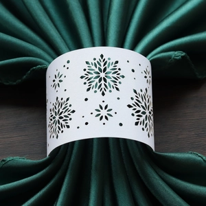 Detail of white laser-cut snowflake napkin ring on dark green silk fabric