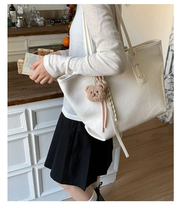 Detail of white crocodile pattern tote bag with teddy bear charm and striped ribbon