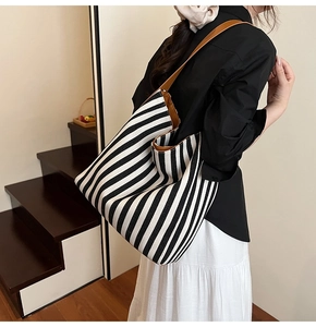 Detail of striped canvas tote bag with brown leather handles worn by a model in a room