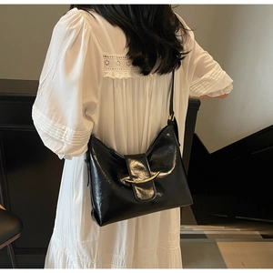 Detail of black glossy hobo bag with crescent gold hardware on a white dress