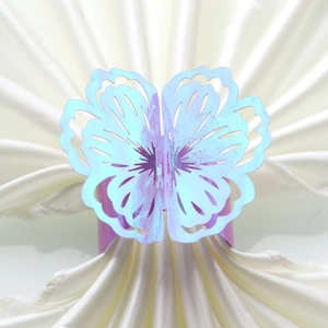 Detailed close-up of a laser-cut iridescent butterfly napkin ring on a beige silk cloth